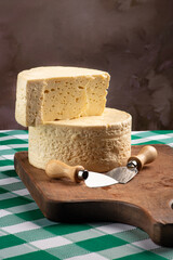 Semi-cured cheese from Brazil arranged on a rustic board on a green and white checkered tablecloth, selective focus.