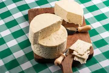 Semi-cured cheese from Brazil arranged on a rustic board on a green and white checkered tablecloth, selective focus.