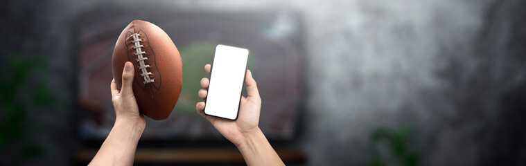 man watching a football game holding a ball and a smartphone - online shopping concept
