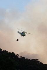 Fototapeta na wymiar A helicopter flies by discharging water amid clouds of smoke from a forest fire