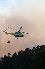 Fototapeta na wymiar A helicopter flies by discharging water amid clouds of smoke from a forest fire