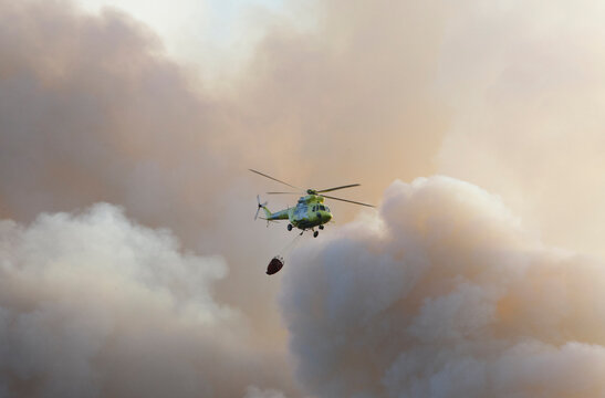 A Helicopter Flies By Discharging Water Amid Clouds Of Smoke From A Forest Fire