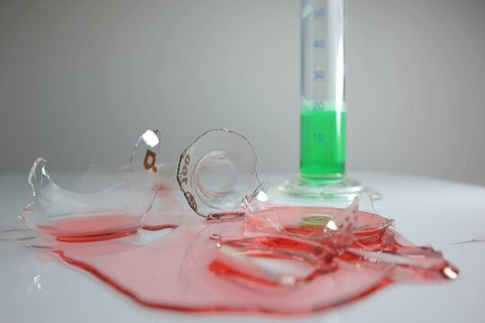 Broken laboratory glass, red liquid chemical spilled from laboratory glassware. Green liquid in measuring glass. Failed lab experiment. Chemical attempt.