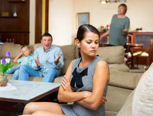 Upset young woman sitting at sofa during quarrelling between family on background at home
