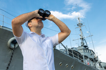 Navy officer standing beside warship and looking around with binocular.