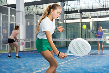 Expressive resolved young fit teenage girl playing paddle ball friendly match on small closed...