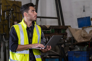 Technical engineer wearing safety vest standing in the factory workplace. Worker holding laptop and looking at machine. Inspection and checking the equipment. Manufacturing and industry concept