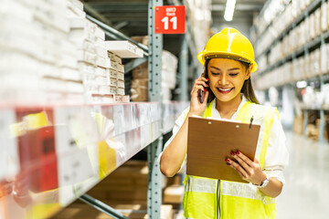Asian woman in helmet and uniform talks on mobile phone discuss amount of stock product inventory...