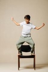 Happy indian boy dancing on an armchair, moving his arms, bending knees.