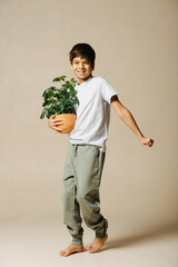 Happy casually dressed indian boy holding a potted plant in his arms