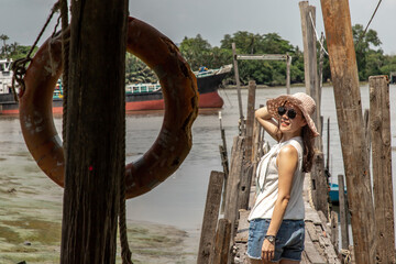 The back of a young woman in casual clothes standing on an old wooden pier and looking at the view...