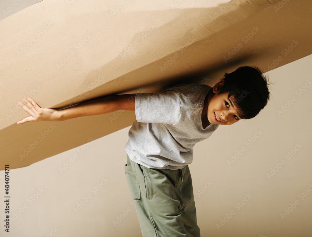 Wall mural ten year old indian boy holding cardboard box on his back twice his size