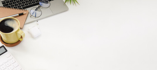 Computer laptop, coffee cup, glasses, calculator and wireless earphone on white office desk.