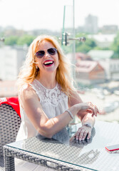 Fototapeta premium A beautiful mature woman in a white blouse sits on a summer terrace and enjoys the weather.