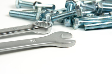 several silver color metal bolts with nuts and wrenches on a white background. close-up and copy space
