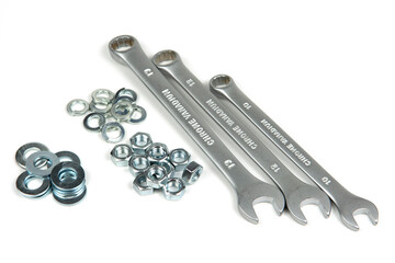 several groups of metal washers and nuts in silver color with wrenches on a white background. close-up