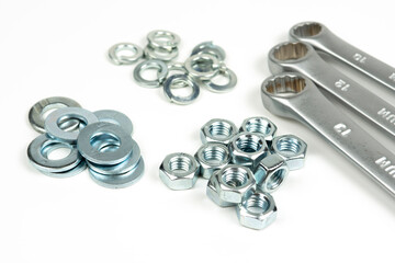 several groups of metal washers and nuts in silver color with wrenches on a white background. close-up