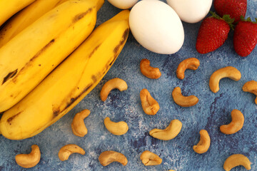 Bananas, eggs, strawberries, and cashew nuts under a blue background. Top view