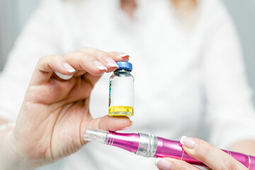 A woman doctor-cosmetologist holds in her hands a device for mesotherapy and an ampoule with a...