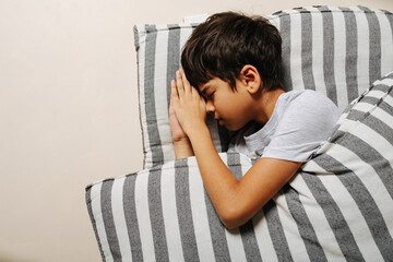 Close up of an indian boy sleeping on a striped mattress under a blanket.