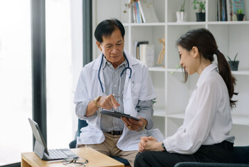 Fototapeta premium Asian male senior doctor explains patient treatment information in digital tablet.