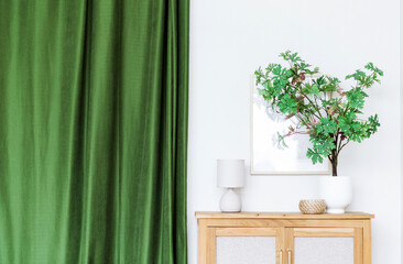 Close-up on stylish vase with green plant on cupboard, lamp and green curtain