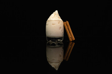 Helado en vaso de cristal decorado con canela, fondo negro, vista elegante con reflejo en cristal. 