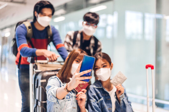 Young happy friend traveler in quarantine for coronavirus wearing surgical mask face protection look at camera making live selfie on smartphone before long travel vacation flight at airport