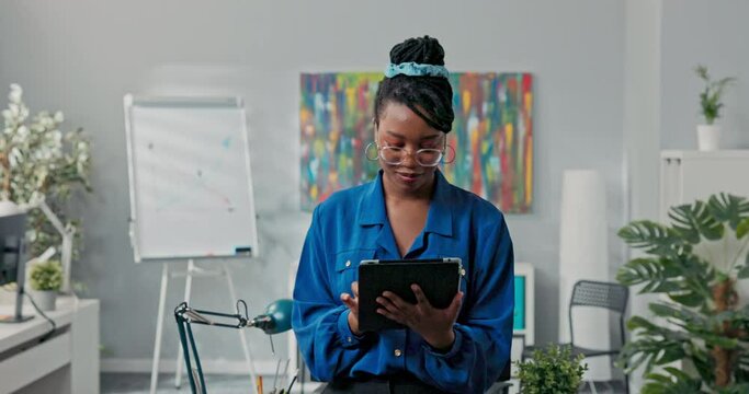 Corporate job corporate duties elegant beautiful ambitious businesswoman stands in office with tablet in hands does report writes back messages empties email inbox, smiles at camera