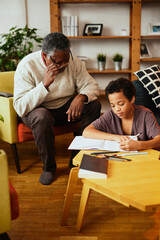 An African-American grandfather is sitting at home with his grandson and helping him with homework.