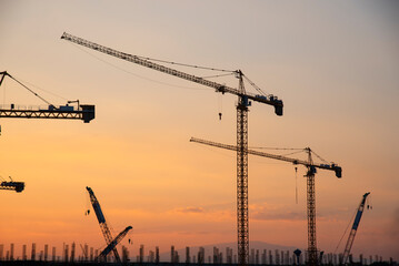 industrial construction cranes and building silhouettes over the sun at sunrise