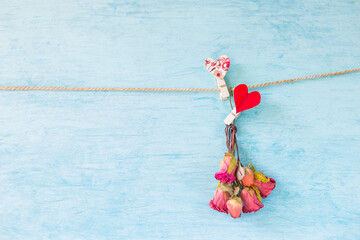 Rose paper flower bouquet with red heart clip hanging on rope with space on blue texture background, valentine greeting card background idea