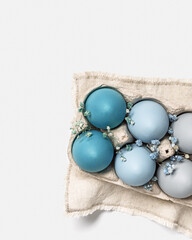 Close up Easter eggs pastel colored in egg box decorated small flowers. Minimal Easter celebration concept, dyed chicken egg with blue green color gradient in carton pack. Top view