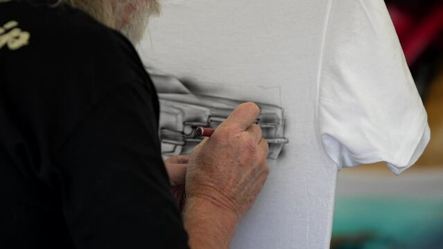 This close up video shows a t shirt being airbrushed by the hands of an artist.