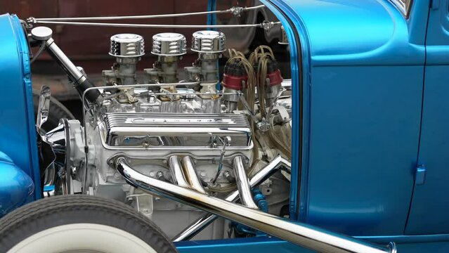 This panning vide shows a close up view of a triple carburetor blue hotrod engine.