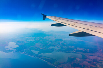 View from the airplane window at a beautiful blue clear sky, earth, sea and the airplane wing