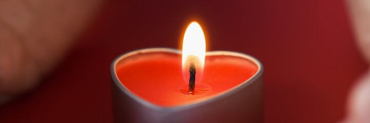 Female hands holding a heart shaped candle in dark closeup