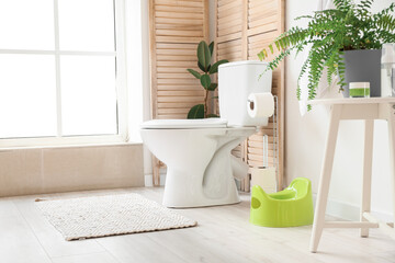Interior of light restroom with green potty, holder with paper rolls and toilet bowl