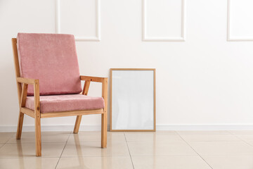Wooden pink armchair and blank frame near white wall