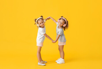Obraz premium Cute little girls in headphones holding hands on yellow background