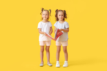 Cute little girls with magazine on yellow background