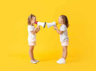 Cute little girls shouting into megaphones on yellow background