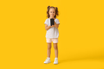 Adorable little girl with mobile phone on yellow background