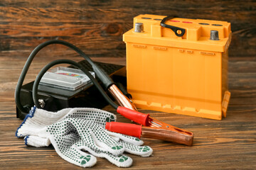 Modern car battery, gloves and tester on wooden background