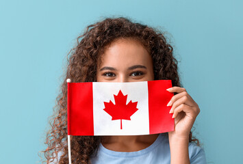 Beautiful young African-American woman with Canadian flag on color background
