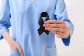 Doctor with black ribbon on light background. Melanoma concept
