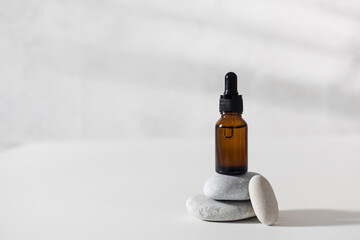 A brown glass dropper stands on stones with a serum for the skin of the face on a light gray background. Care cosmetics.