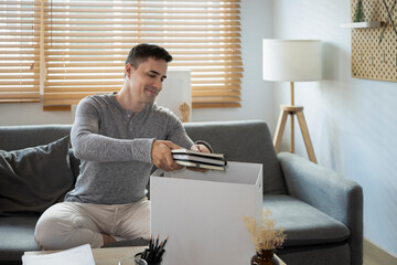Happy young man sitting on couch and preparing personal stuff for removal day.