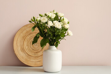 Vase with bouquet of beautiful roses on table near light wall