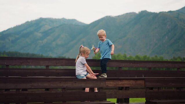 Little boy presents small bouquet to elder sister on benches